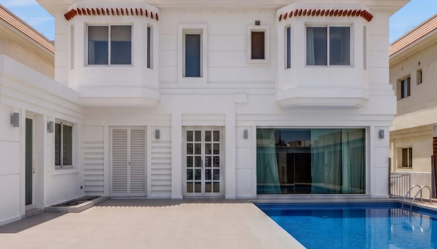 A modern two-story white house with large windows and sliding glass doors, featuring a swimming pool and spacious poolside patio under a clear blue sky.