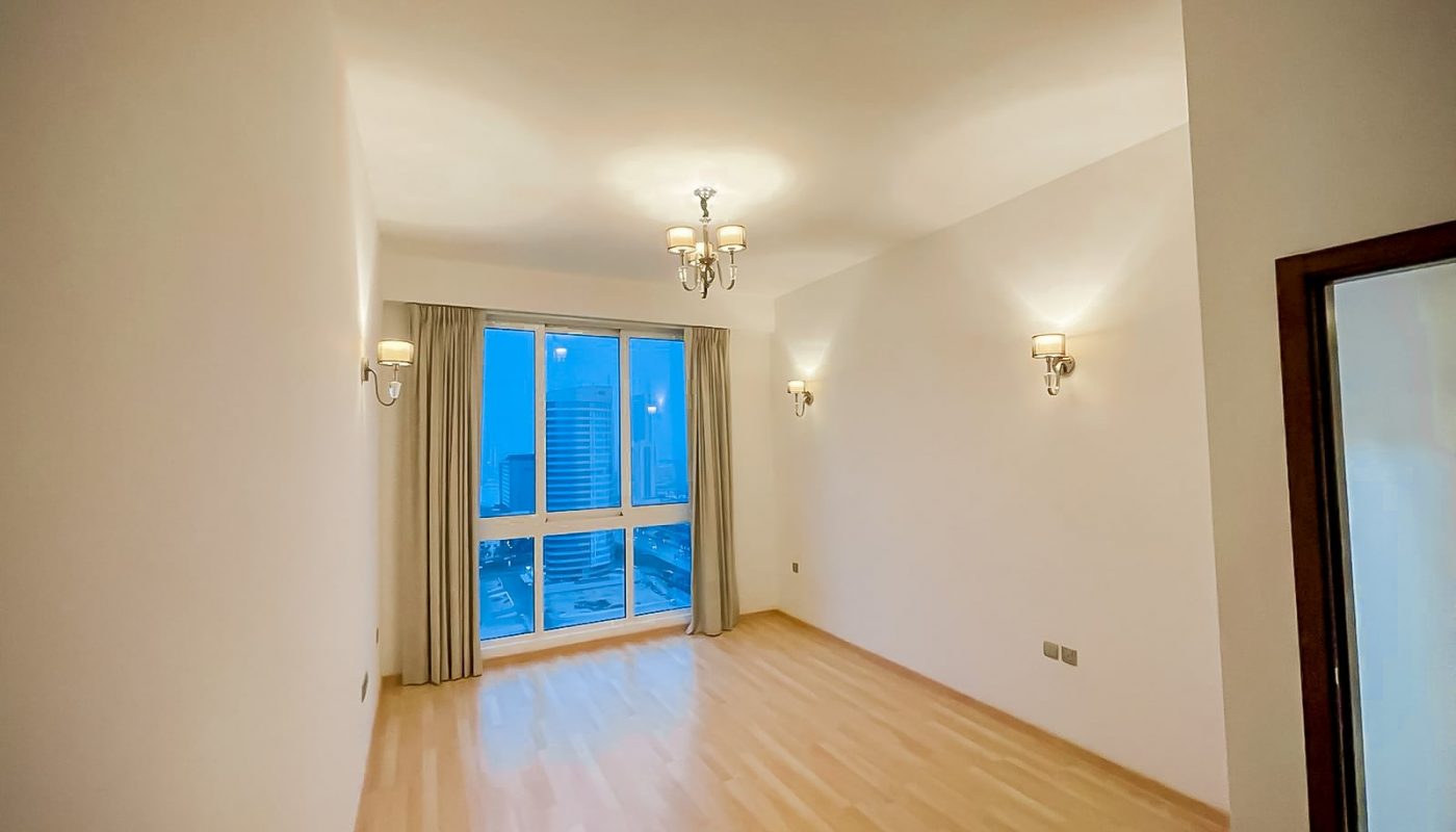 A spacious room with wooden floors and a large window.