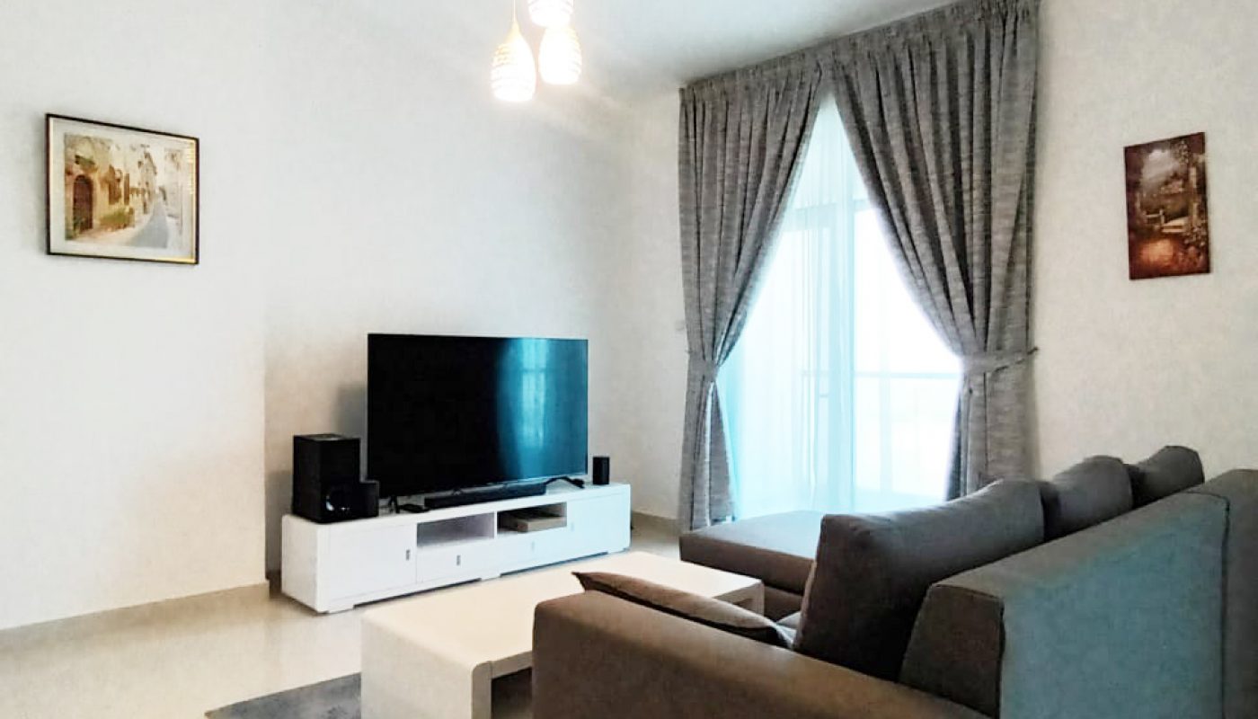 Modern living room with a gray sofa, white coffee table, TV on a white stand, gray curtains over a large window, and two framed pictures on white walls.