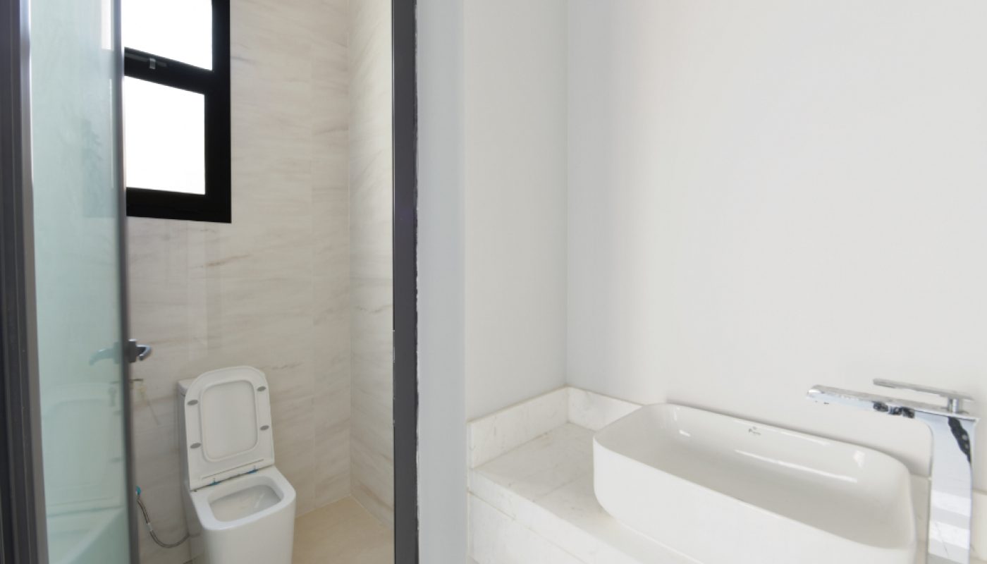 A modern bathroom with a white toilet next to a window and a separate white countertop with a rectangular sink and faucet.