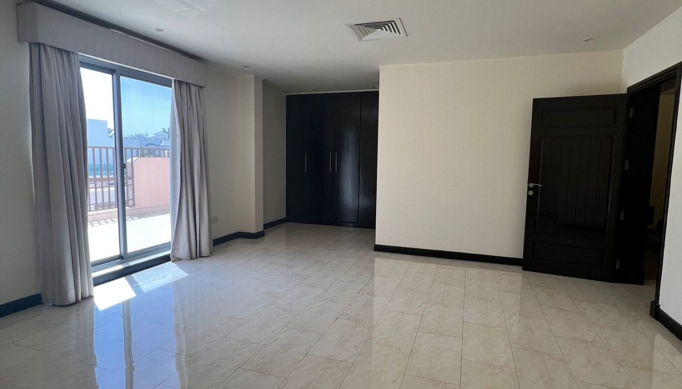 Spacious empty room with tiled floor, large window with curtains leading to a balcony, and dark built-in wardrobes against one wall.