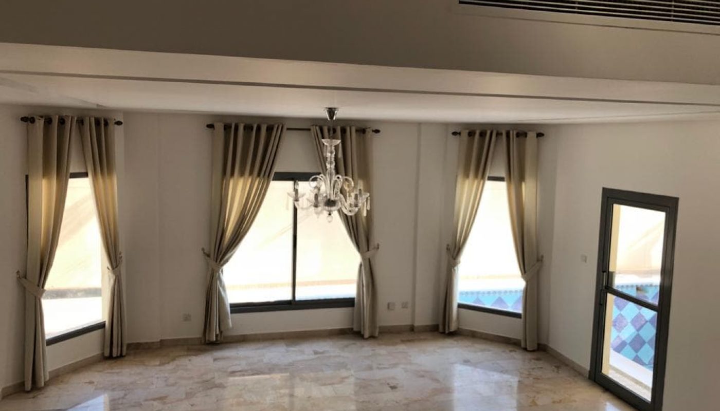 Empty living room with marble floors, draped windows, a chandelier, and a pool view through a door on the right.