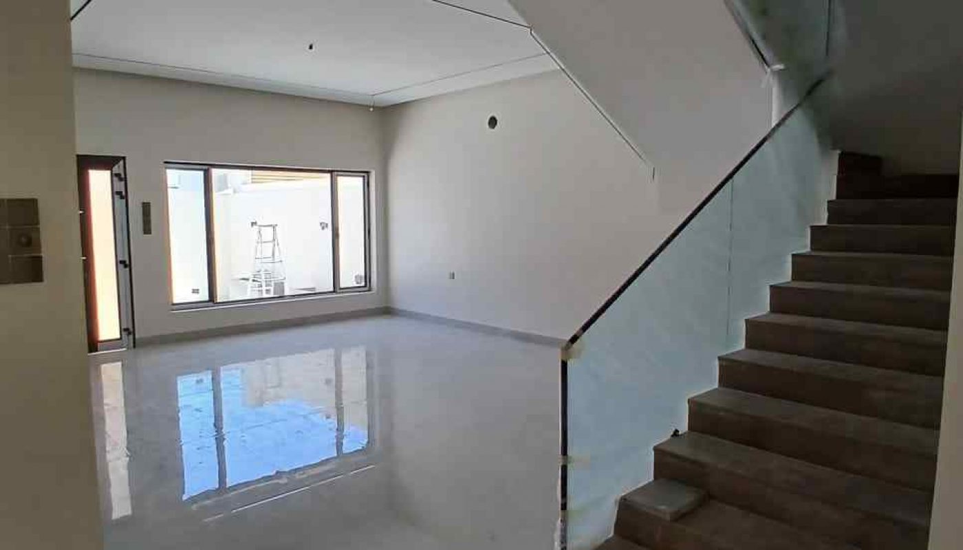 Modern, unfurnished interior showing a tiled living area with large windows, a glass-paneled staircase, and neutral-colored walls and floors.