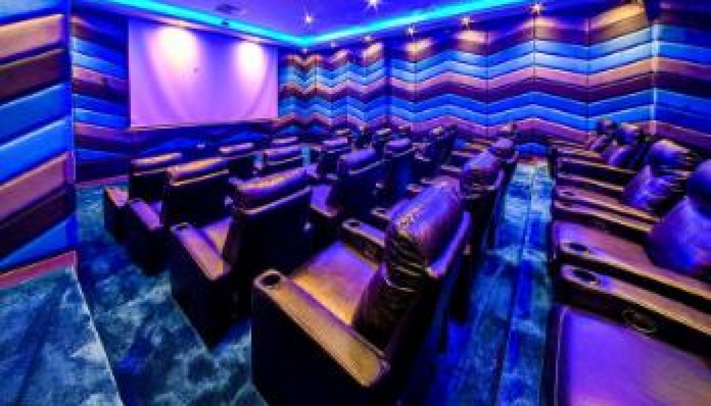 A small movie theater with recliner seats, blue and purple lighting, and a blank screen at the front.