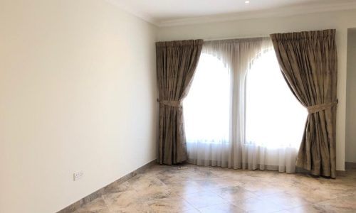 A bright, empty room with tiled floor, light-colored walls, and two large windows with double-layered curtains drawn to the sides.