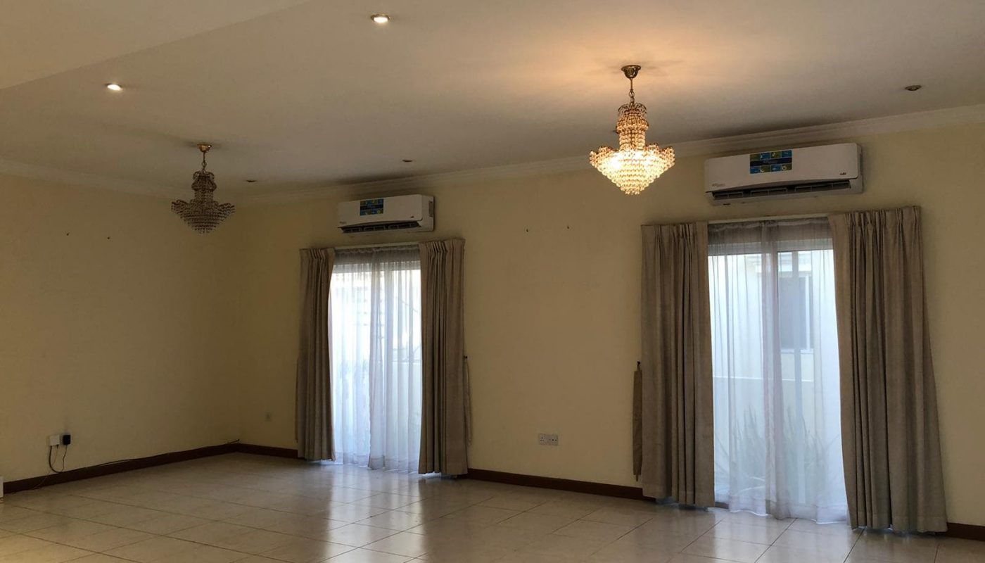 Empty villa living room with tiled floor, two chandeliers, air conditioner, and curtains on windows.
