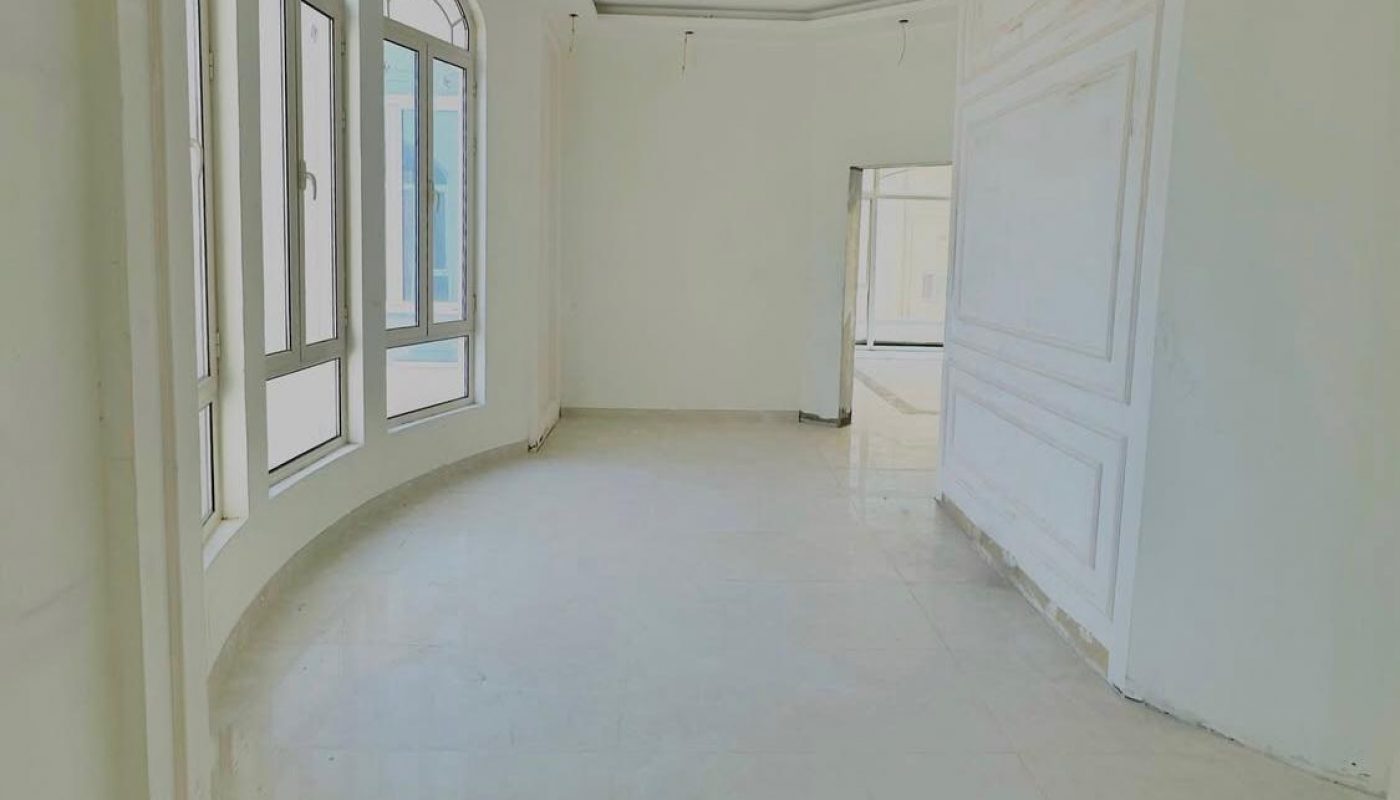 Empty, unfurnished room with white walls, large arched windows, glossy tiled floor, and natural light entering from the left side.