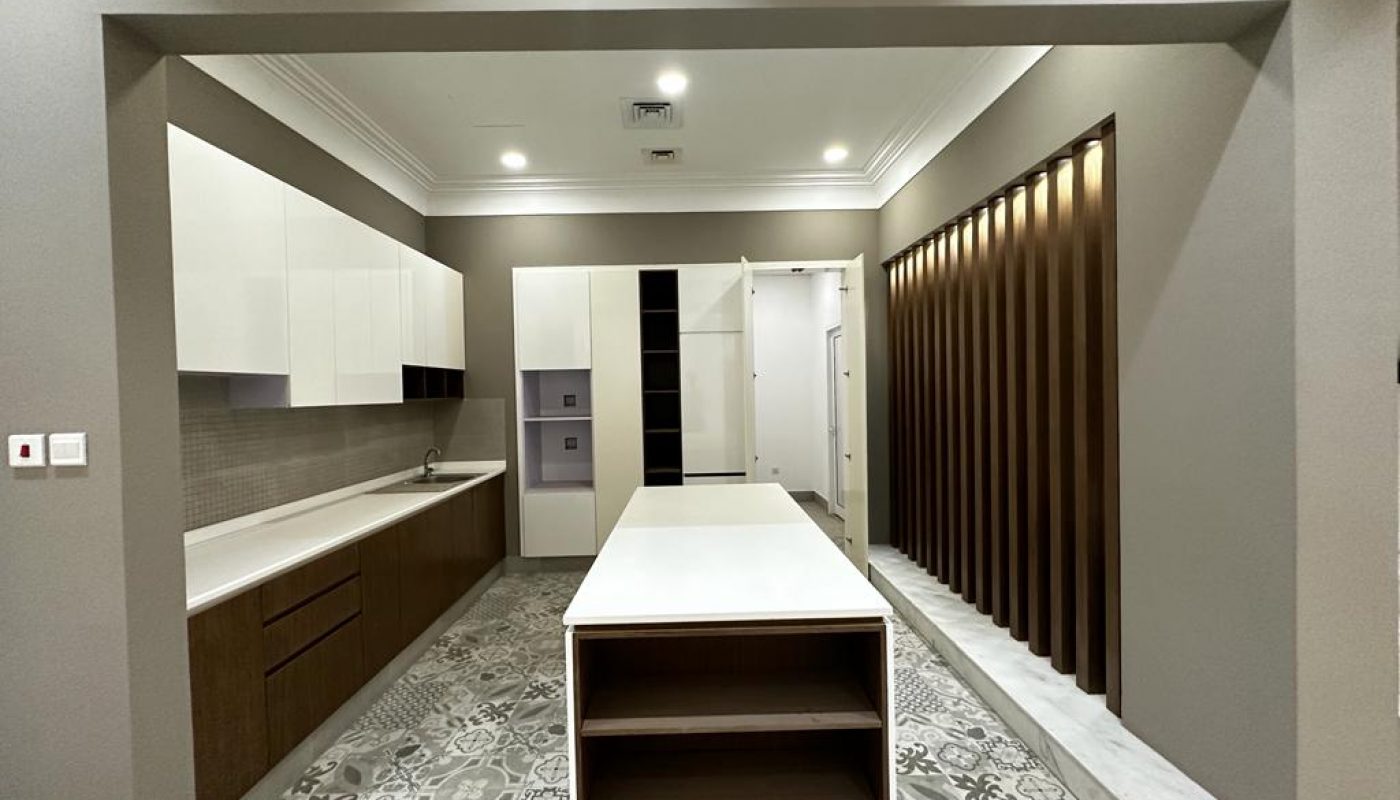 Modern kitchen with an island, patterned tile flooring, white and brown cabinets, vertical wooden slats, and built-in appliances. Overhead recessed lighting brightens the space.
