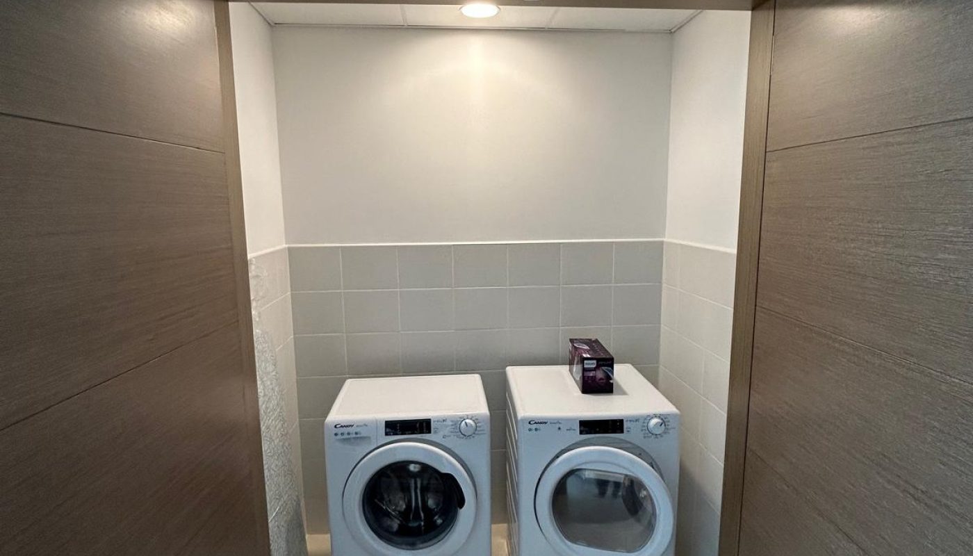 A laundry area with a washing machine and a dryer side by side, enclosed by wooden sliding doors and lit by a ceiling light.