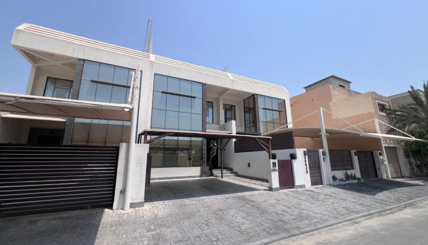 Modern two-story house with large glass windows, covered parking areas, and a paved driveway under a clear blue sky.