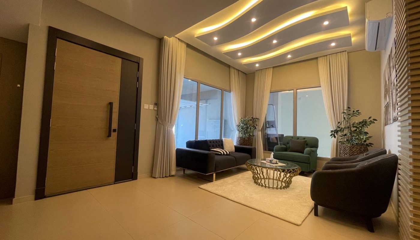 Modern living room with contemporary furniture, large windows, decorative ceiling lighting, potted plants, and a neutral color palette.