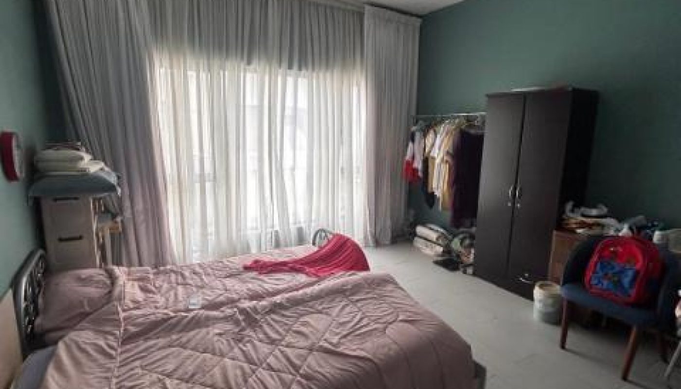 A bedroom with two beds, a wardrobe, a clothing rack, and a chair.