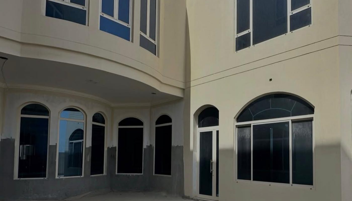 A modern two-story house with large arched windows, a glass door, and an empty, unfinished pool in the courtyard.