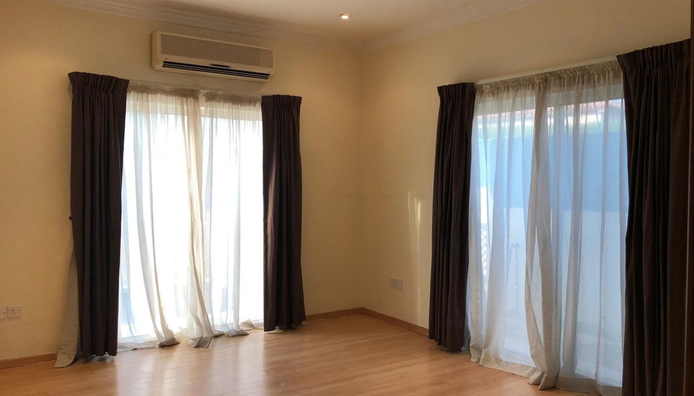 Semi-Furnished living room with hardwood floors, white walls, sheer curtains, dark drapes, and an air conditioning unit on the wall.