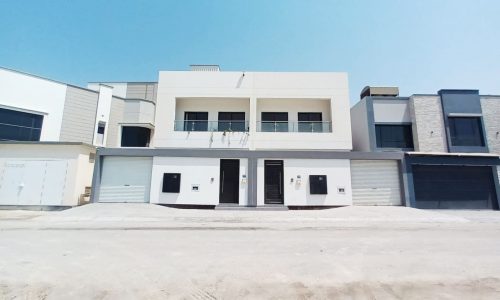 A modern white building with two garages in front of it, featuring a garden.