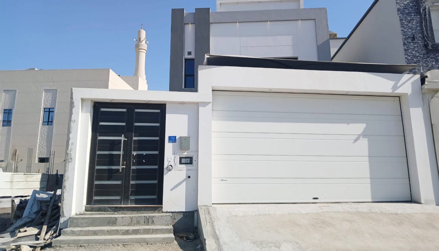 Contemporary 3BR Villa exterior under clear skies, featuring a garage door on the right and front door with sidelight on the left, alongside construction debris.