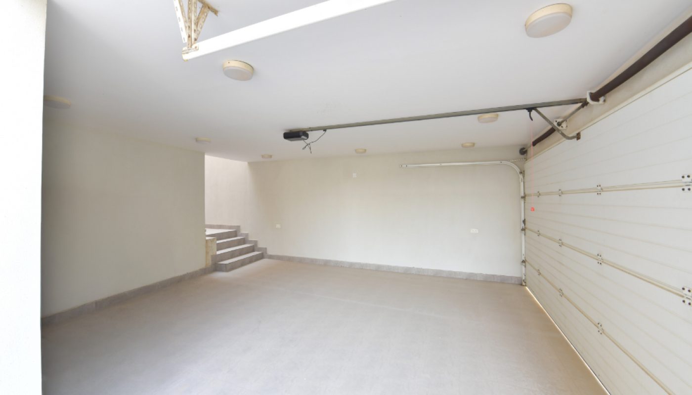 An empty, clean garage with a white automatic door, tiled floor, and a set of steps leading up to an interior door on the left.