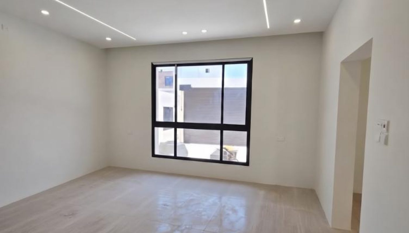Empty modern room with large window, white walls, recessed ceiling lights, and tiled floor.