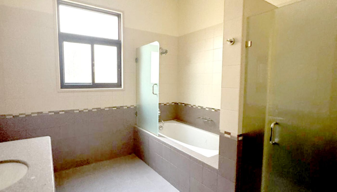 A bathroom with tiled floor, bathtub, glass shower enclosure, countertop with sink, and a window allowing natural light.