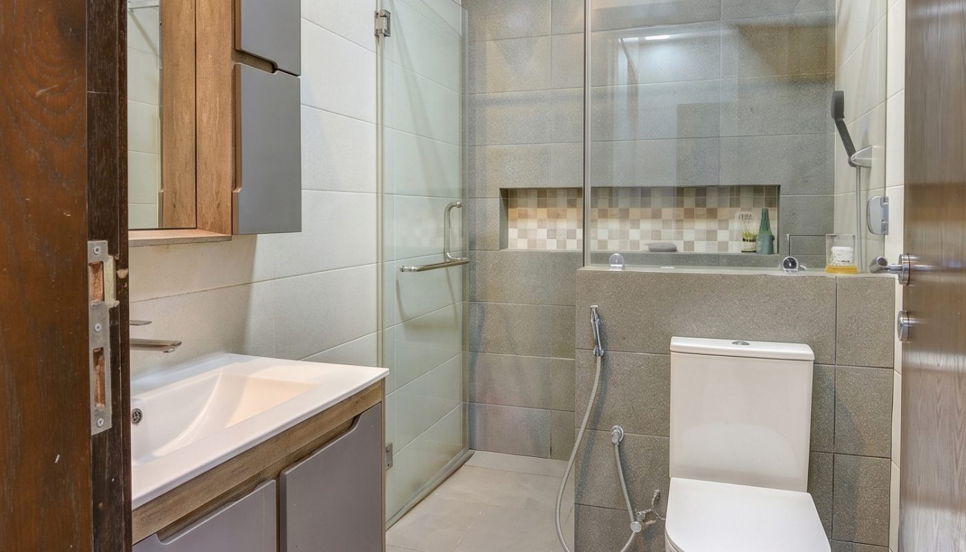 Modern bathroom with a wall-mounted sink and cabinet, glass shower enclosure, toilet, handheld bidet, and tiled walls and floor.