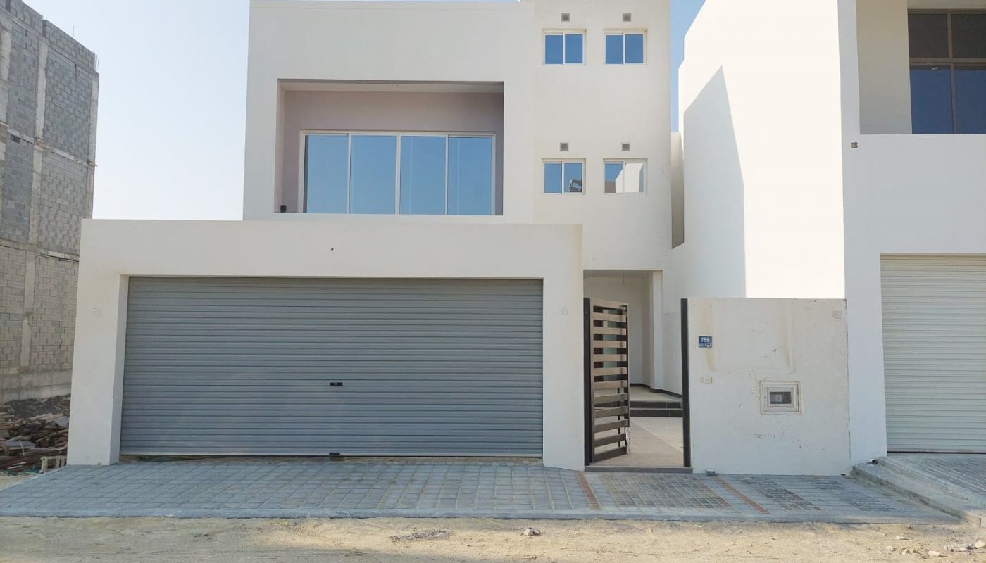 A white house with a garage in front of it, for sale in Durrat Al Muharraq, featuring 2 roads.