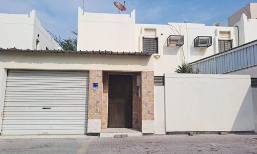 A white villa with a garage door in front of it in Hamad Town for sale.