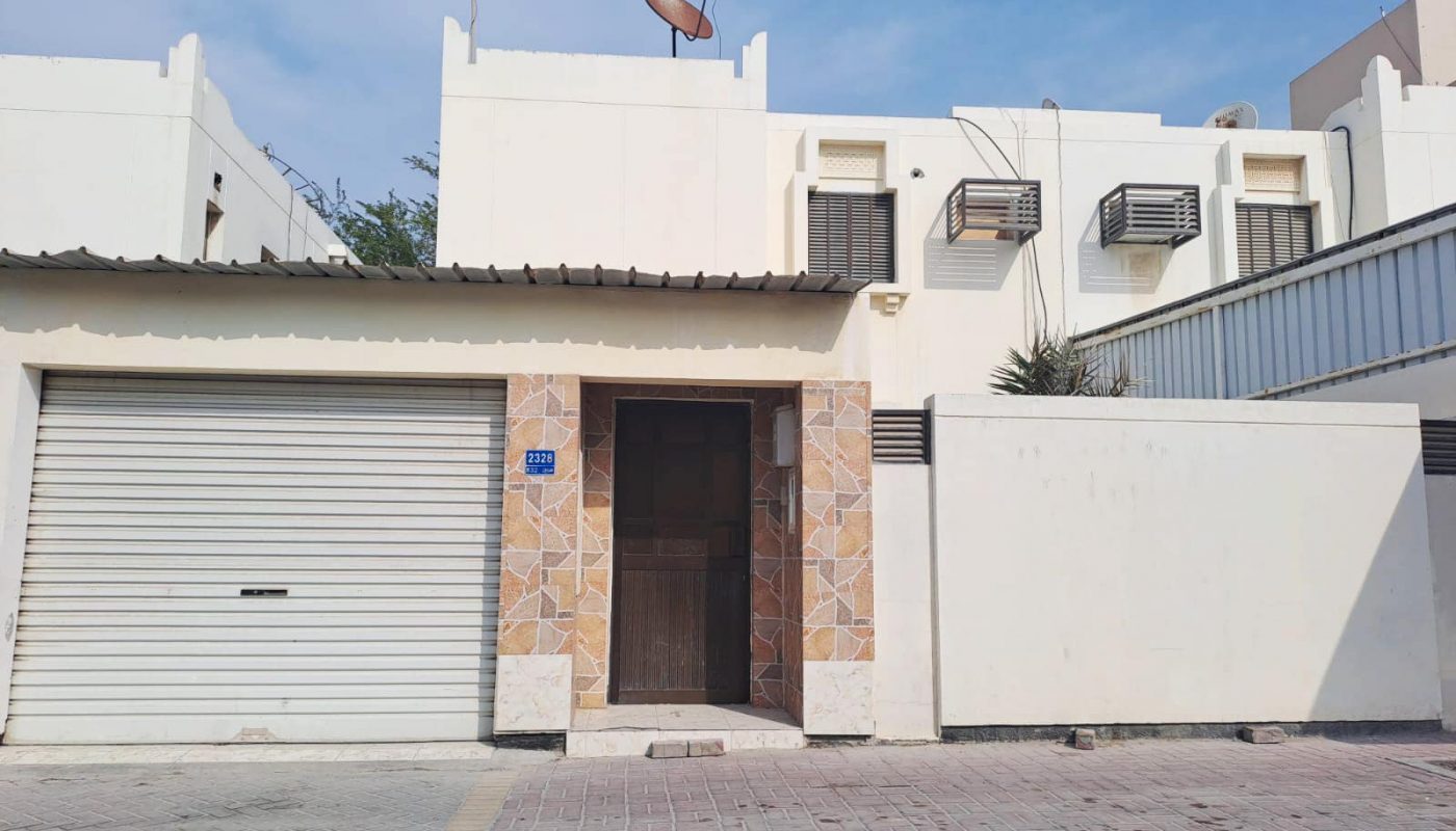A white villa with a garage door in front of it in Hamad Town for sale.