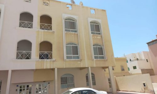 A white car is parked in front of a real estate building for sale in Juffair.