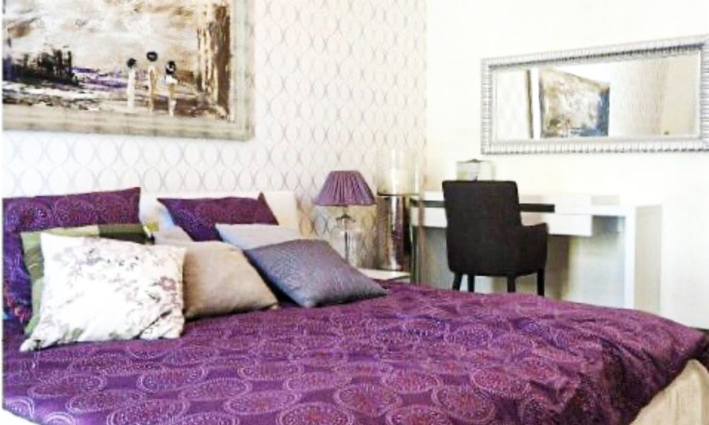 An amazing purple and white bedroom with a bed and a dresser in an apartment for sale that requires maintenance.