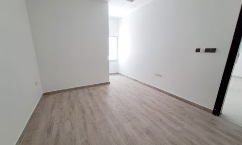 An empty and cozy room with wood floors and white walls for sale in Hidd.