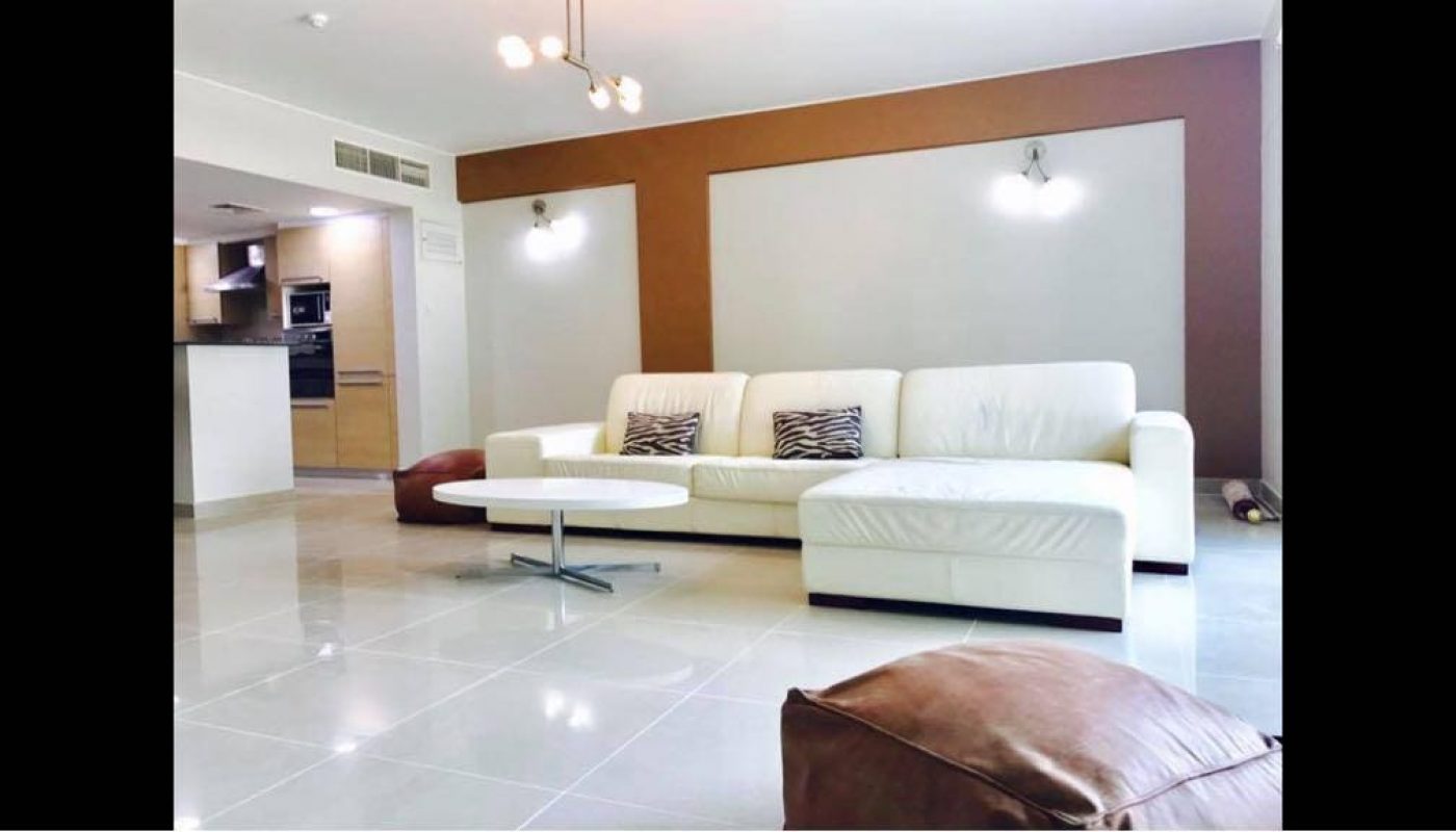 A fully furnished living room with a white couch and coffee table in an apartment for rent in Amwaj Islands.