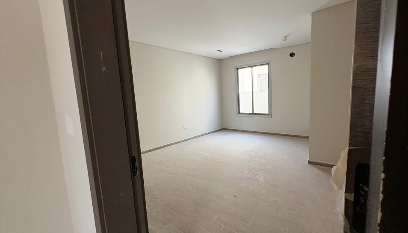 Empty, unfurnished room with tile flooring, beige walls, a window, and recessed ceiling lights viewed from an open doorway.