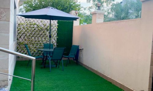 A small backyard with artificial grass and a table and chairs in a Wonderful 5BR Villa for Sale in Muharraq.