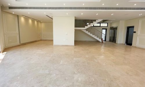 Spacious, unfurnished room with beige tiled floor, recessed ceiling lights, and a modern staircase leading to an upper level. Walls are cream-colored with decorative molding. Large windows provide natural light, creating the perfect auto draft of brightness throughout the space.