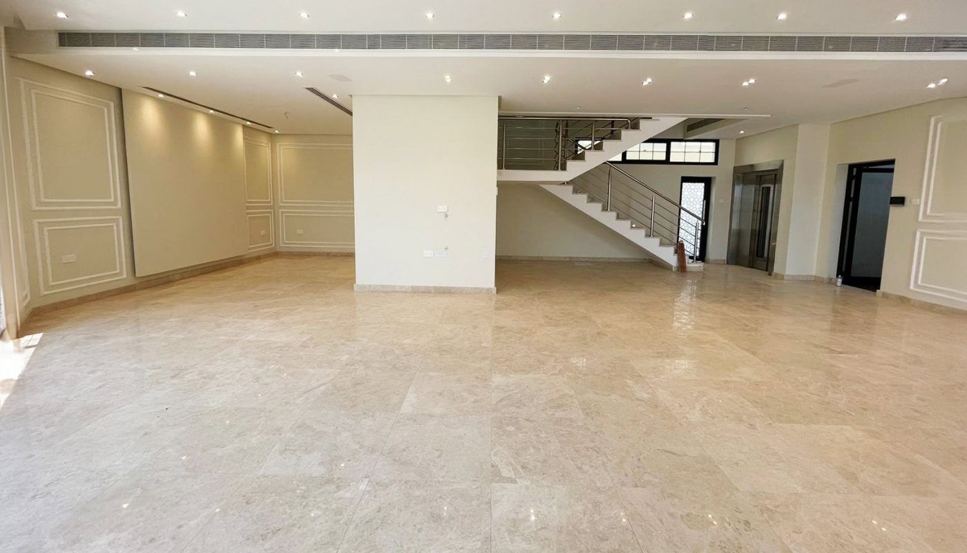Spacious, unfurnished room with beige tiled floor, recessed ceiling lights, and a modern staircase leading to an upper level. Walls are cream-colored with decorative molding. Large windows provide natural light, creating the perfect auto draft of brightness throughout the space.