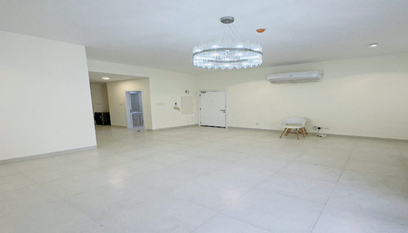 Spacious, unfurnished room with white tiled floor, white walls, a chandelier, split air conditioner, single chair, and a closed white door.