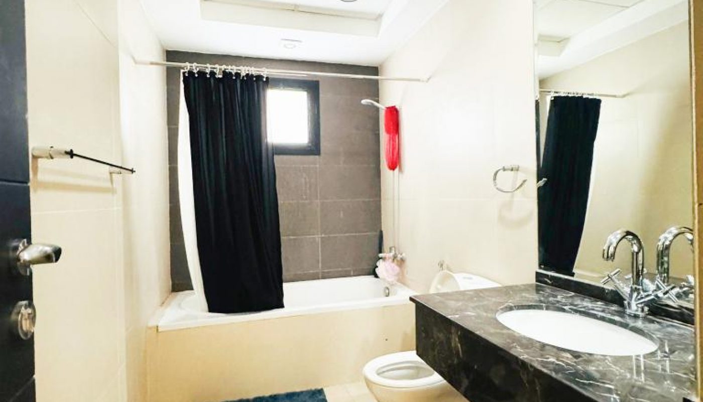 Modern bathroom with a bathtub and black shower curtain, toilet, wall-mounted sink with large mirror, and tiled floor with blue mats.