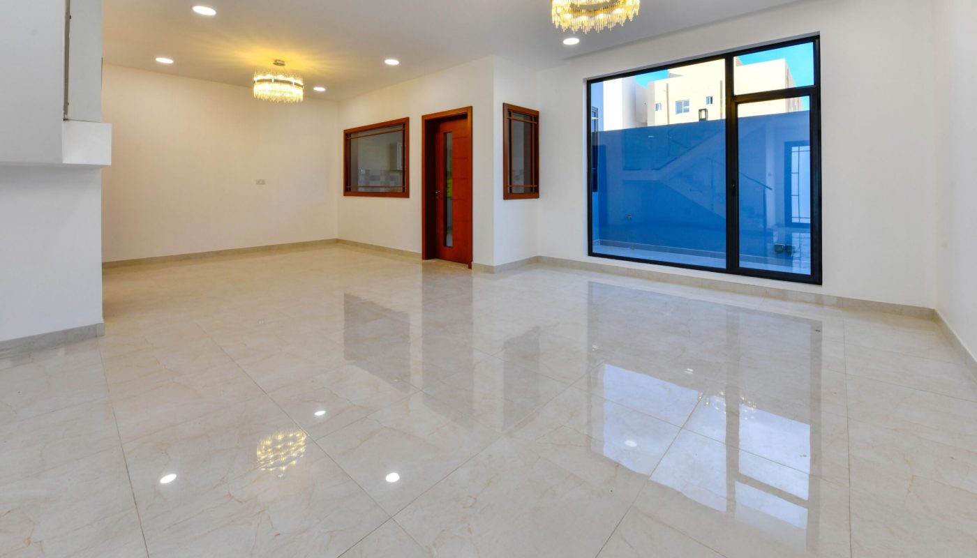 Spacious empty room with glossy tiled floor, white walls, large window, two chandeliers, and recessed ceiling lights.