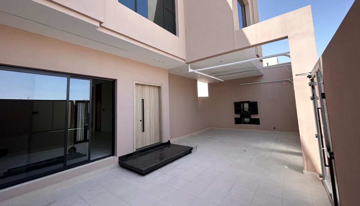 A modern, two-story building with large windows and an open, tiled courtyard under a clear sky.