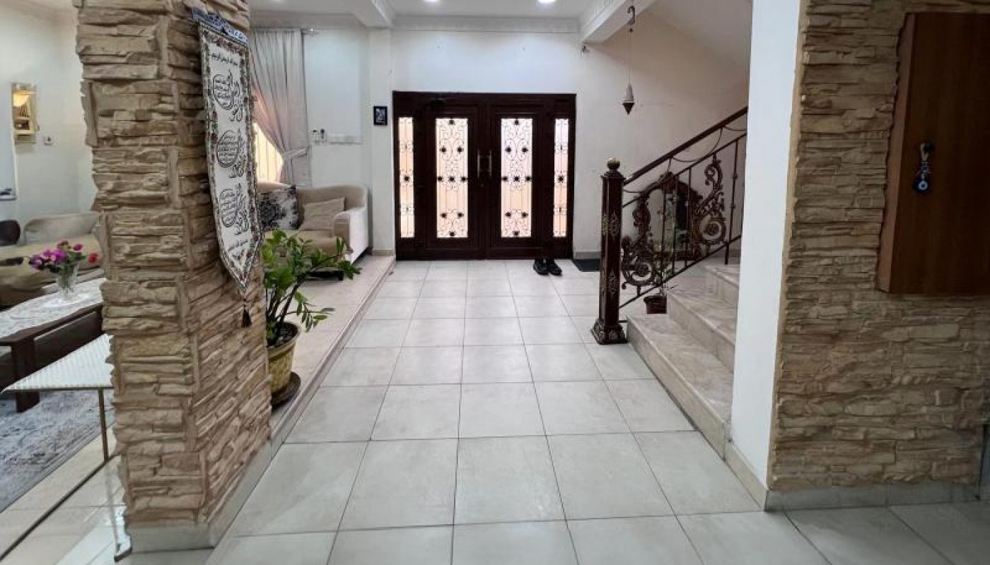 A spacious hallway with tiled floors, stone wall accents, a staircase with a railing on the right, and double front doors with glass panels at the end.