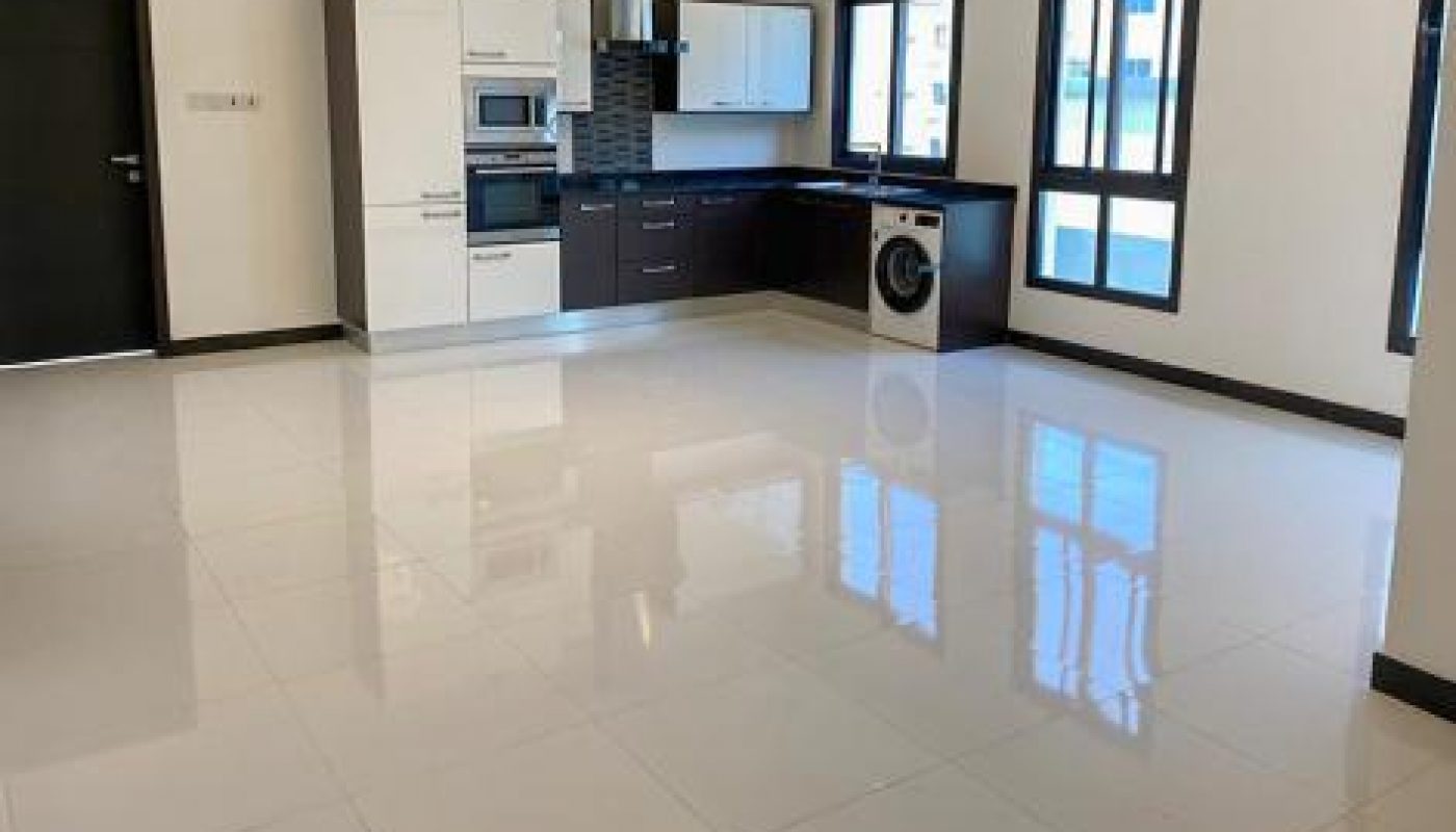 Spacious, modern open-plan kitchen and living area with glossy white tile floors, black cabinets, large windows, and a washing machine.