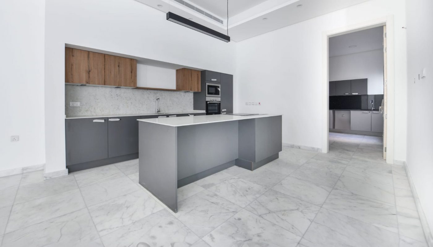 Spacious modern kitchen with large island, marble floors, white walls, and wooden cabinets. Recessed lighting and a long hanging light fixture accent the room.