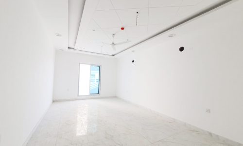 An empty room with white walls and a ceiling fan in a luxury apartment for sale in Riffa.