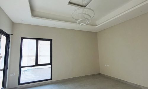 An empty, unfurnished room with light-colored walls, a tiled floor, a large window, and a ceiling light fixture awaits your design plans. Perfect for an auto draft of ideas to make this space uniquely yours.