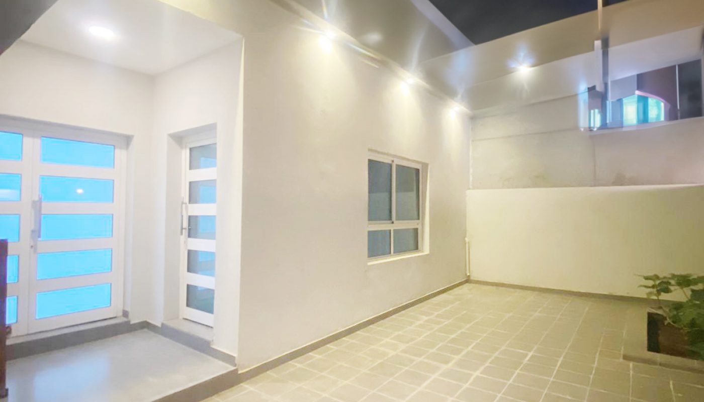 Modern house entryway and courtyard at night, featuring tiled flooring, white walls, glass doors, a window, recessed ceiling lights, and a small plant in the corner.