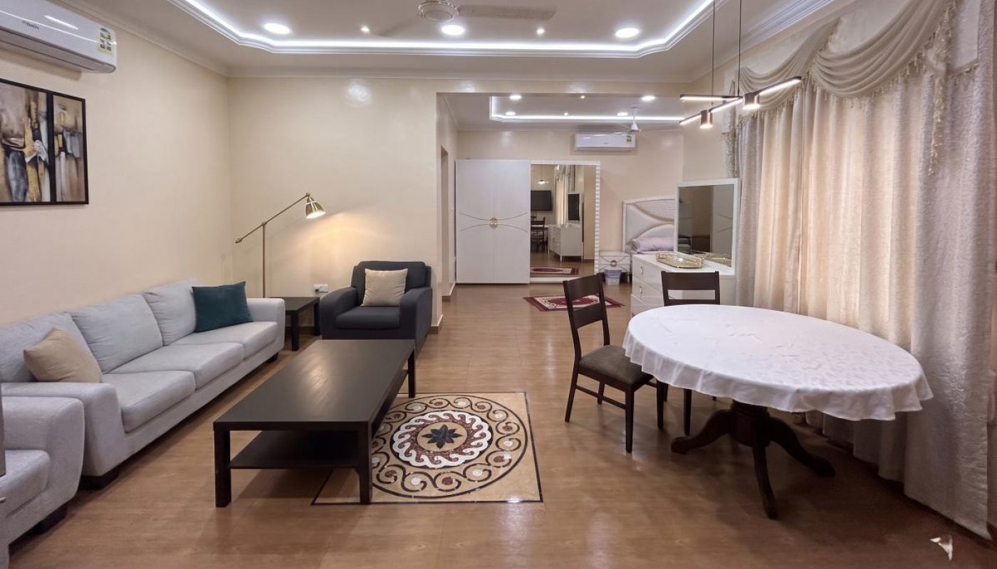 A well-lit living and dining area with a sofa set, coffee table, dining table with chairs, ceiling fan, and recessed lighting.
