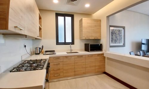 Modern kitchen interior featuring wooden cabinets, a gas stove, microwave, and a small window, with bright, natural lighting and an Auto Draft system.