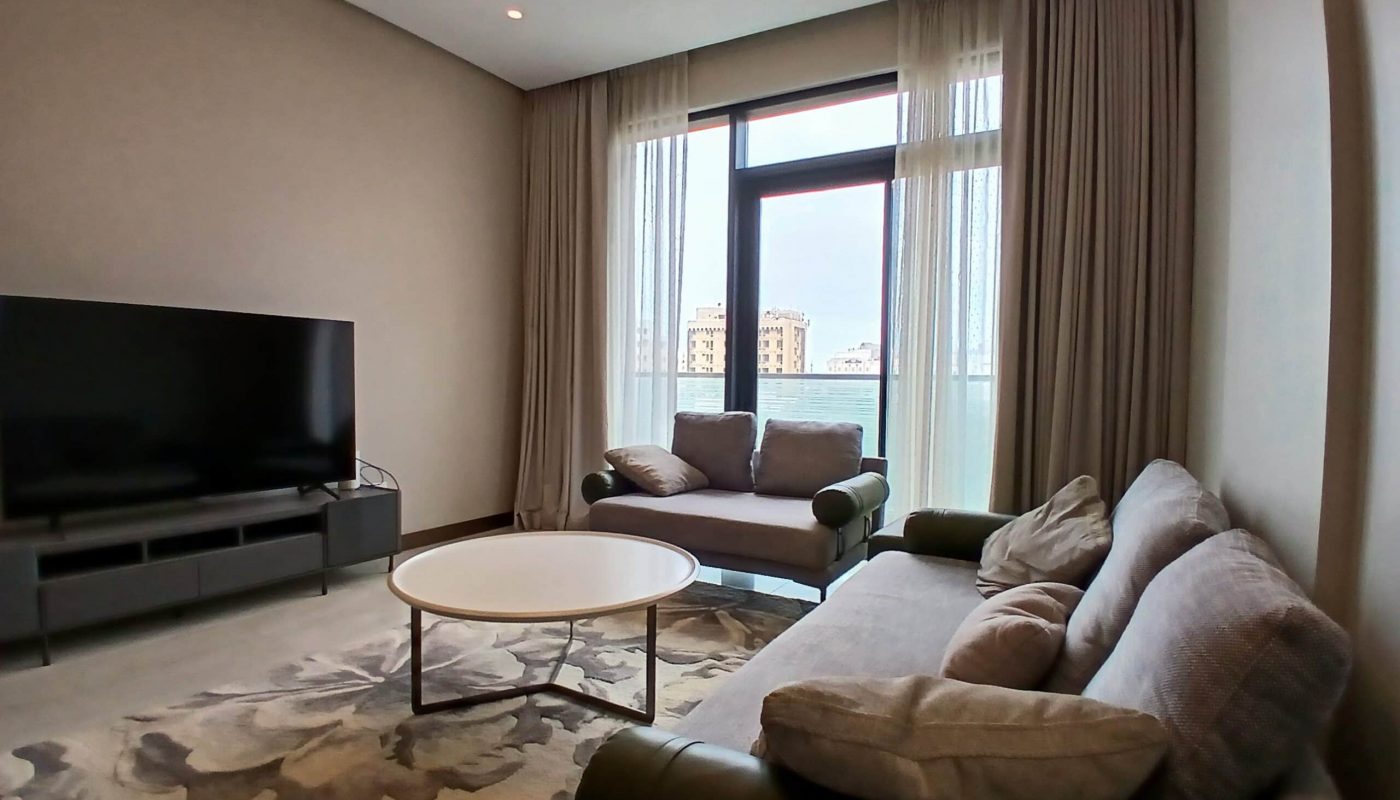 Modern living room with a large window, luxury contemporary furniture including a sofa and armchair, a round coffee table, and a flat-screen TV.