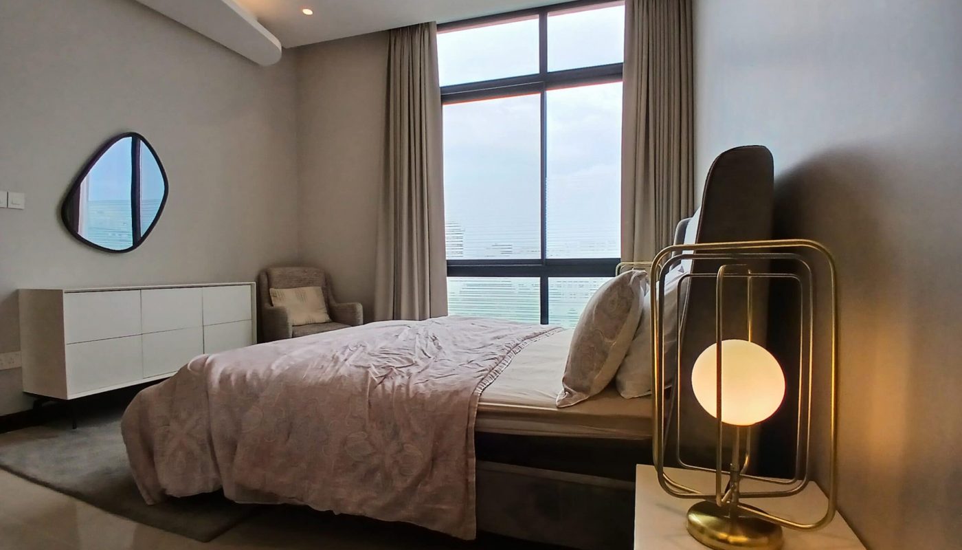 Modern spacious bedroom with a large bed, bedside lamp, mirror, and windows with curtains, showing a serene, well-lit interior.