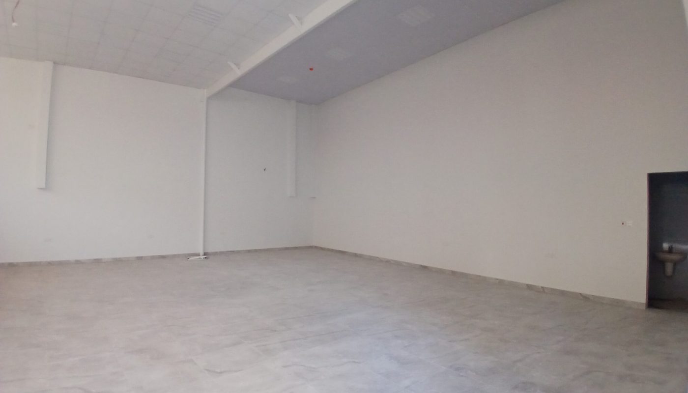 Empty commercial space with gray tiled floor and white walls, showing auto draft ceiling lights and a small door on the right.